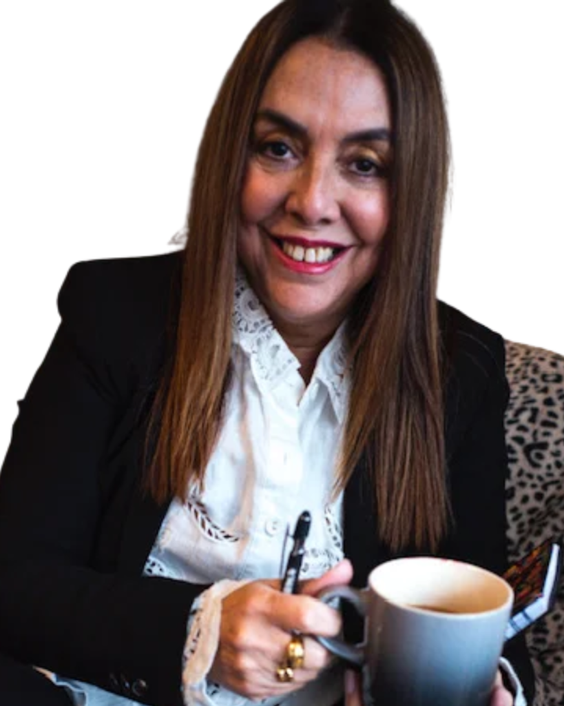Smiling woman with long brown hair in a blazer and lace blouse, holding a mug and scissors.