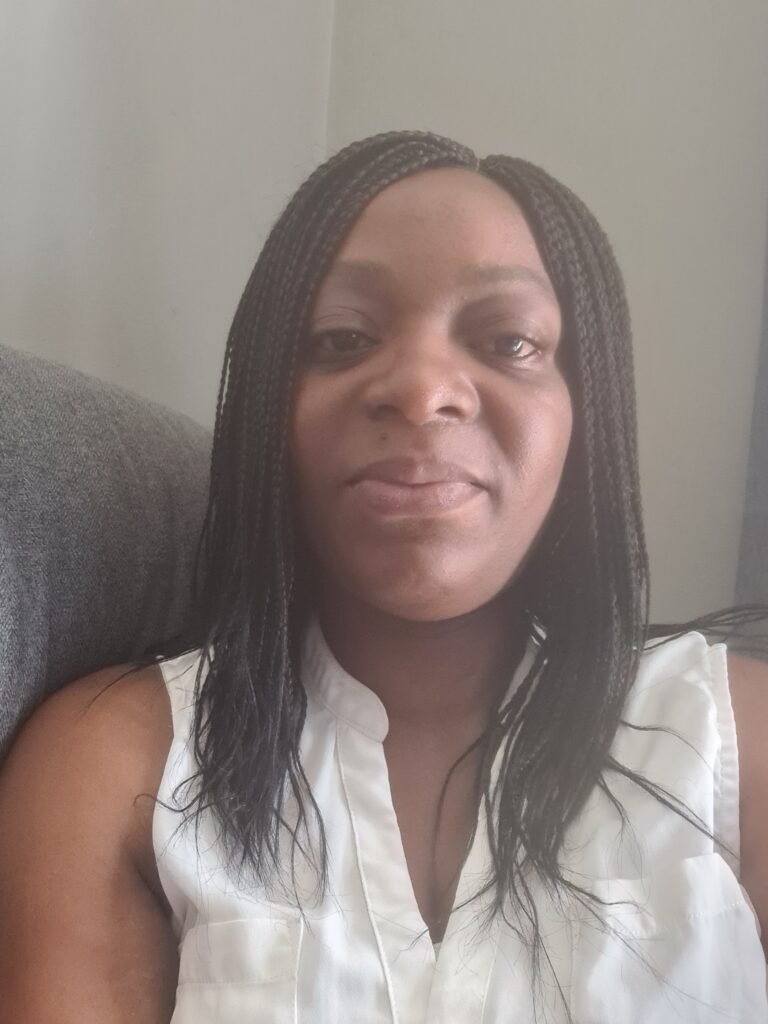 Close-up of a woman with braided hair wearing a white sleeveless top, sitting on a gray couch against a neutral wall.
